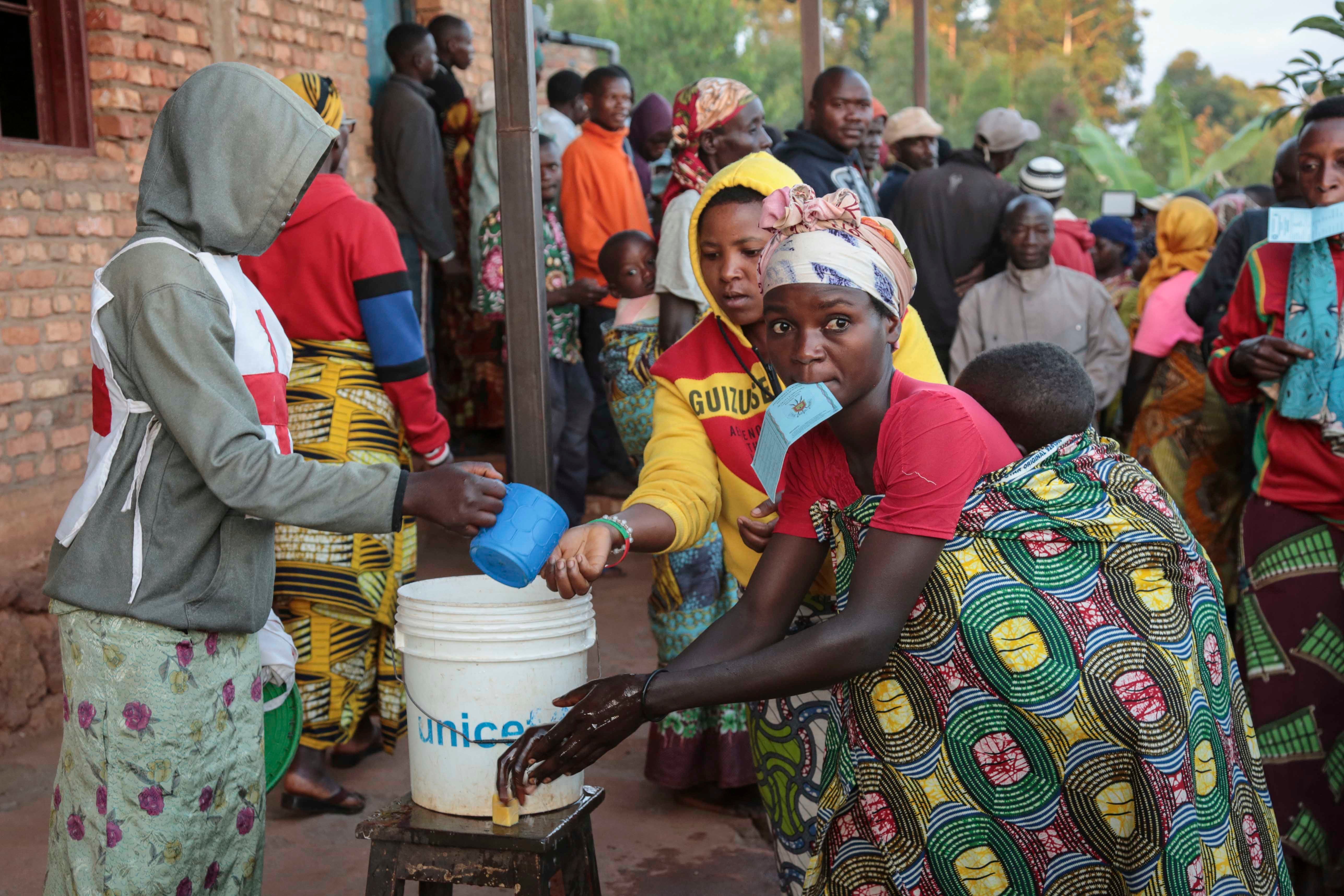 A voter holds her identity card in her mouth as she washes her hands before casting her vote in the presidential election, in Giheta, Gitega province, Burundi, on May 20, 2020.