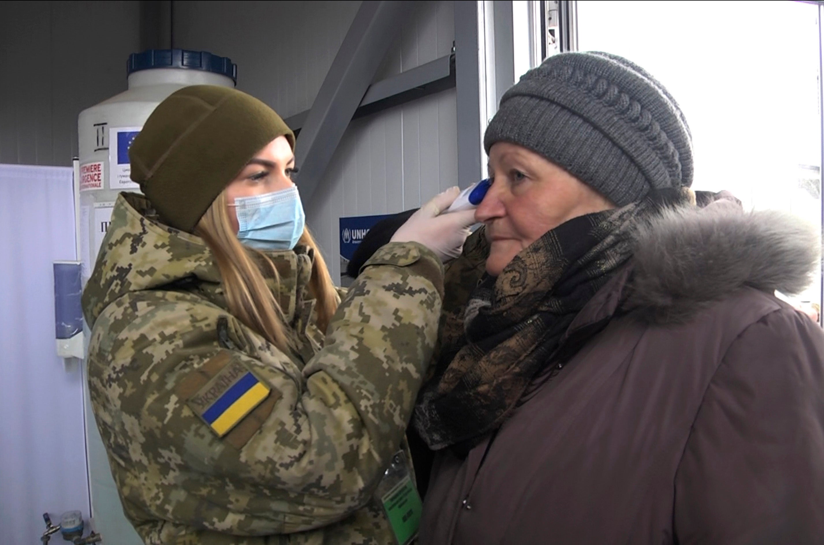 A soldier in a face mask checks the temperature of an older woman at a checkpoint in Mayorsk, Donetsk region, Ukraine, Monday, March 16, 2020.