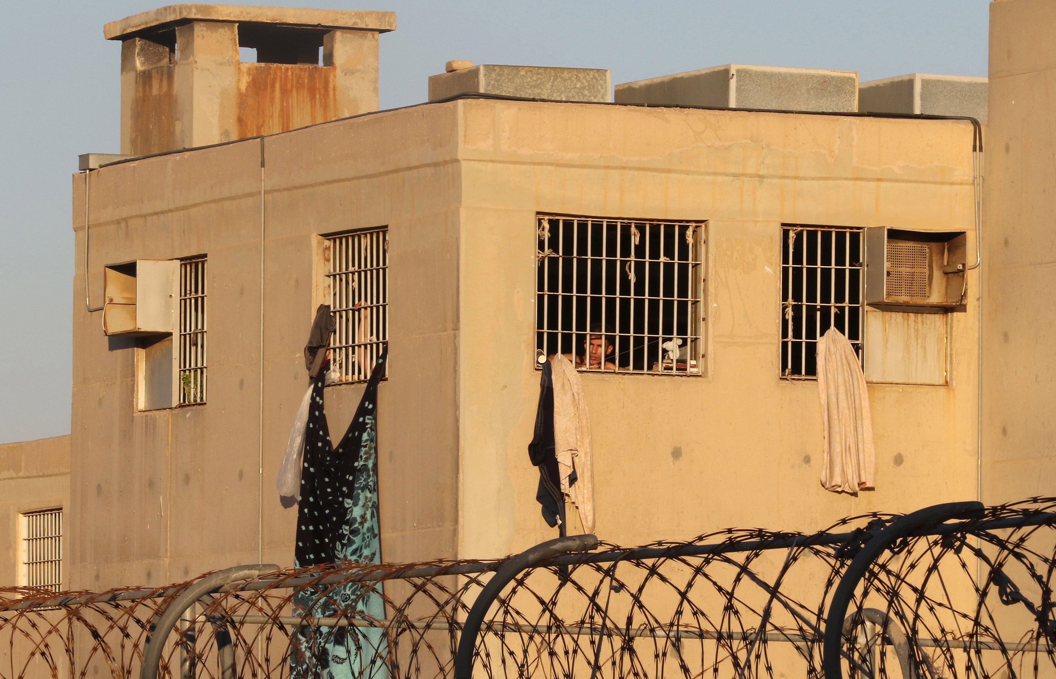 A man looks out from behind the bars of a prison building