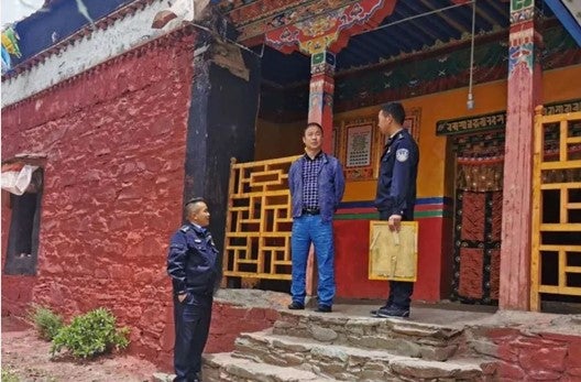 A man and two uniformed police officers stand on the steps of a monastery