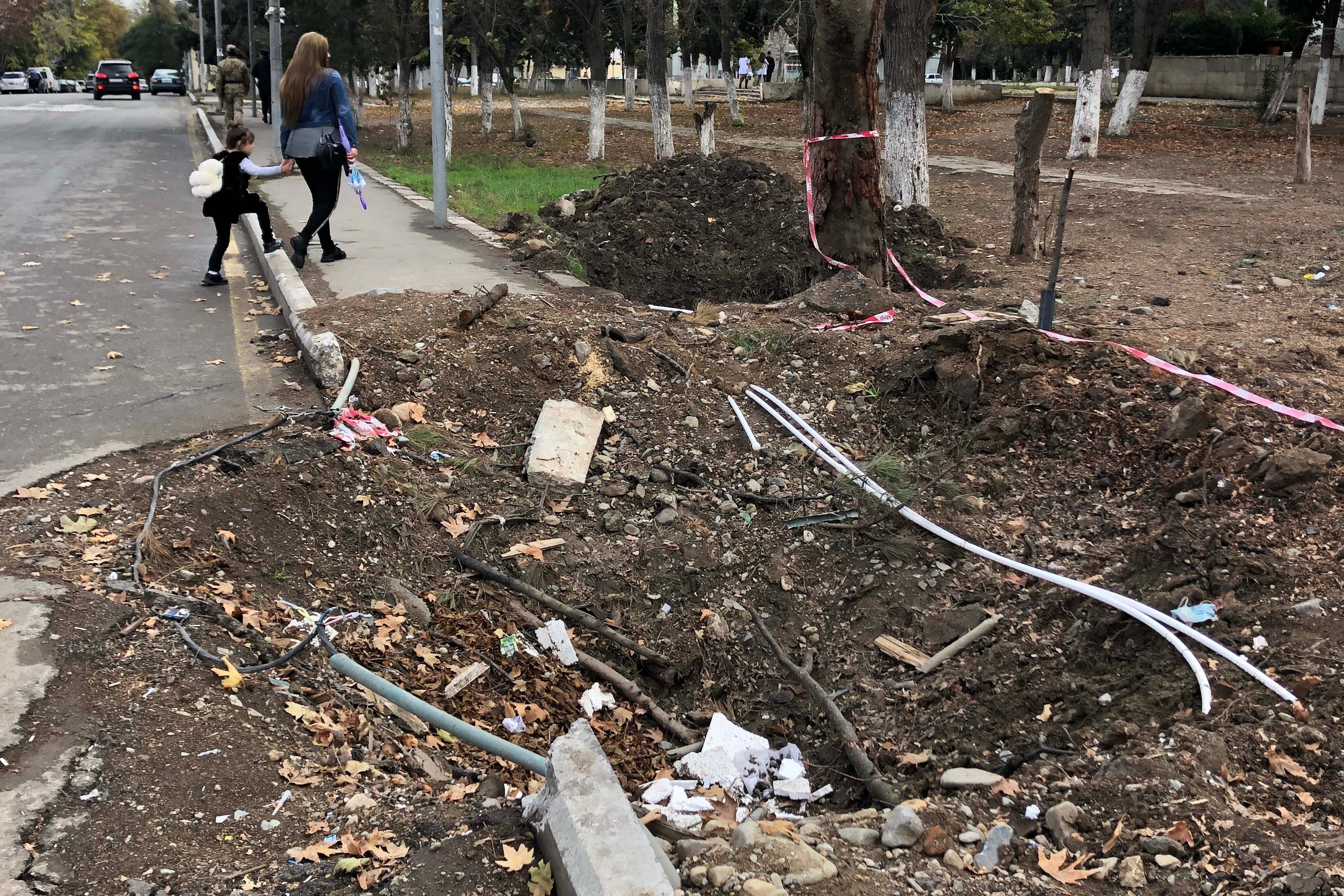 A woman and child walk past a crater in a road
