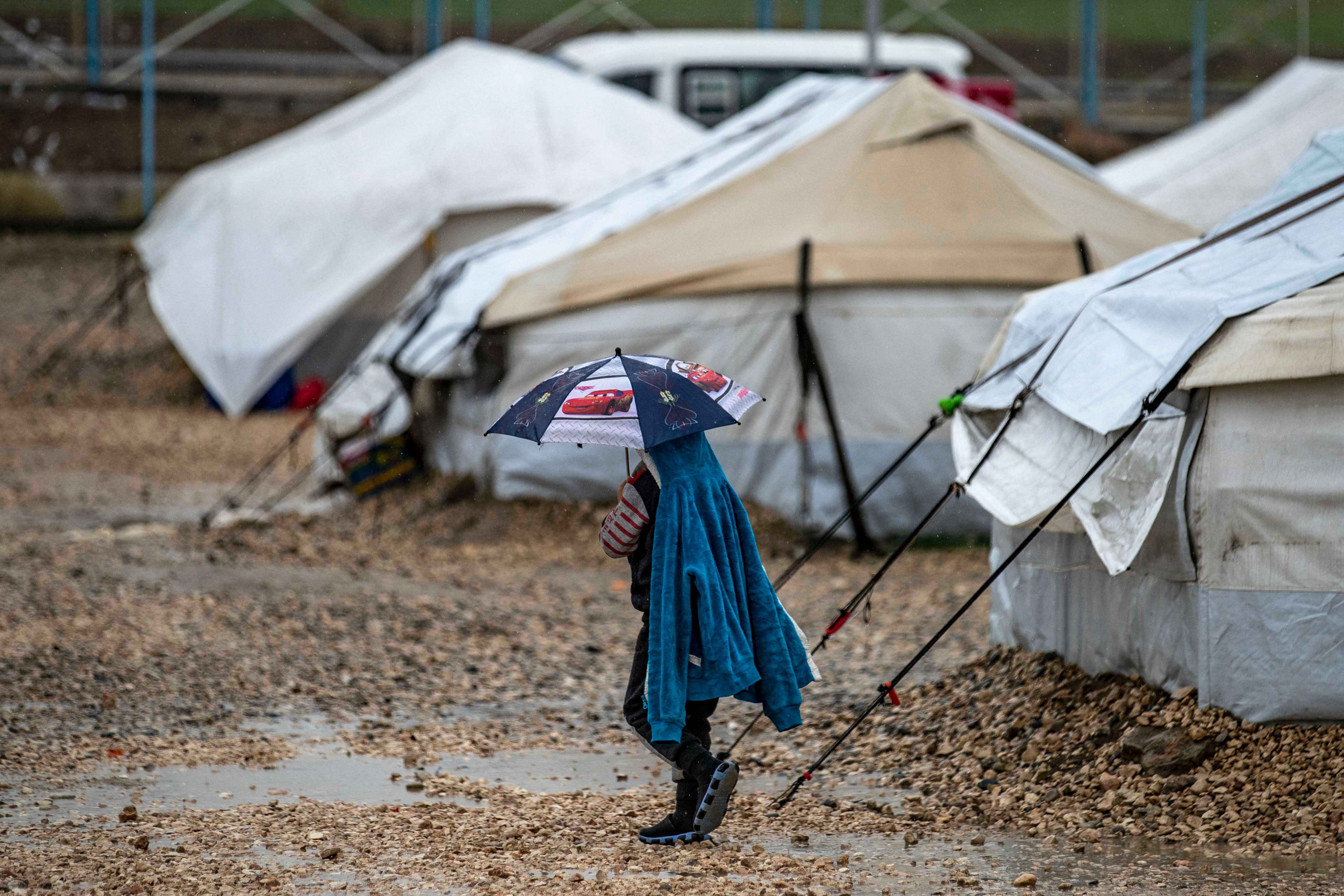 A young person holds an umbrella as he walks in the rain at Camp Roj, where relatives of people suspected of belonging to the Islamic State (IS) group are held, in Syria's northeastern Hasakah province, on March 4, 2021. 