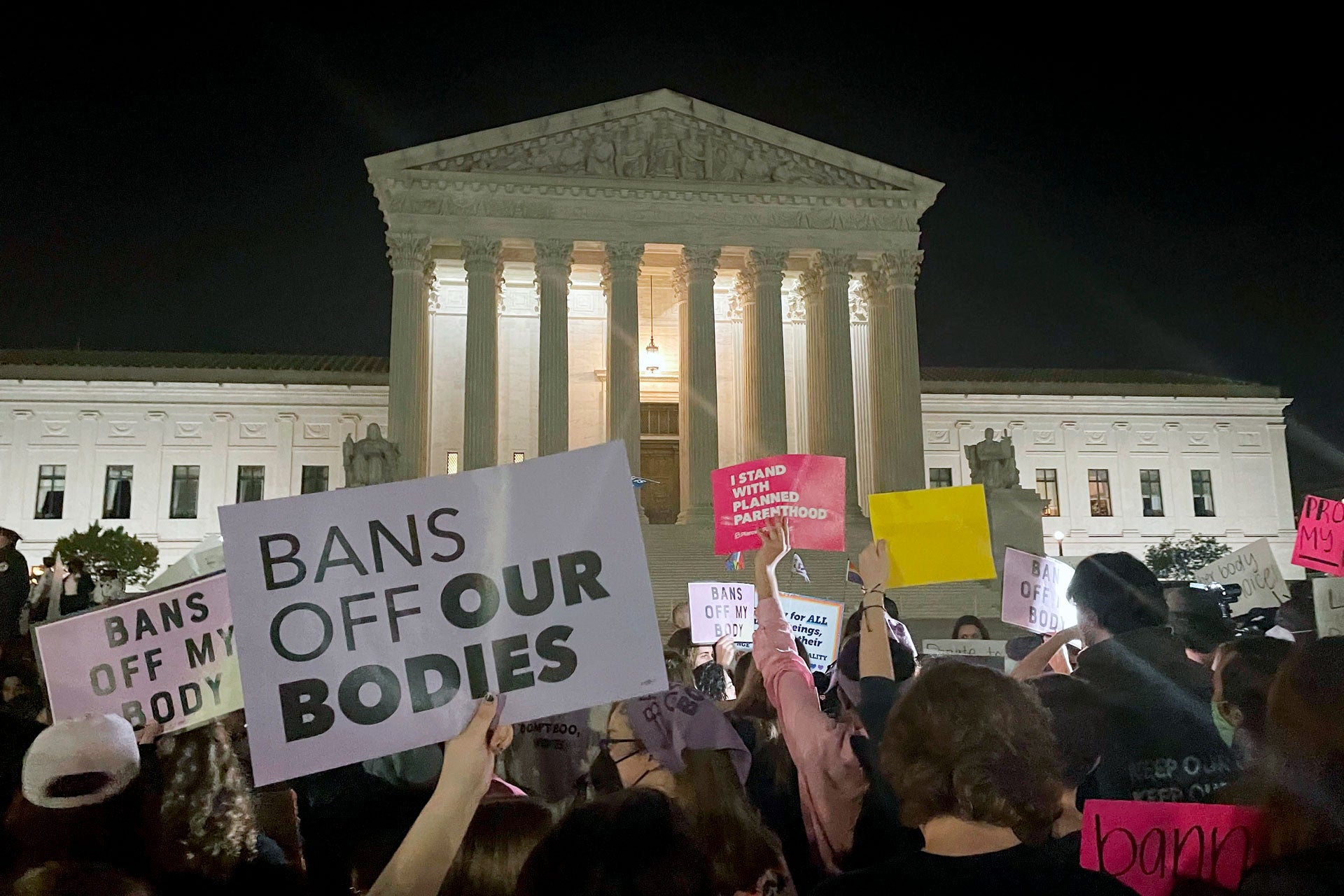 People protest holding signs outside of the US Supreme Court at night