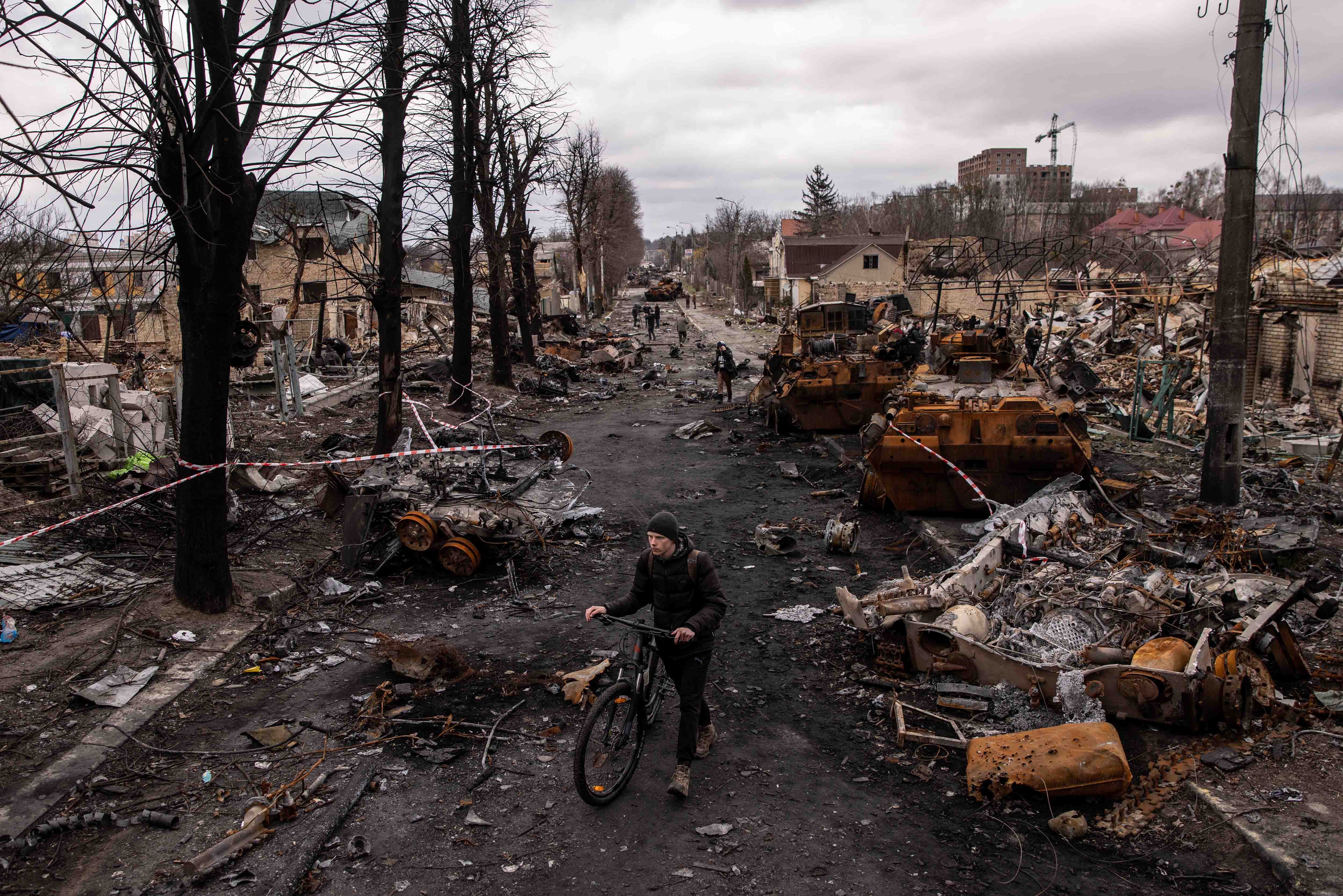 A man pushes his bike through debris and destroyed military vehicles
