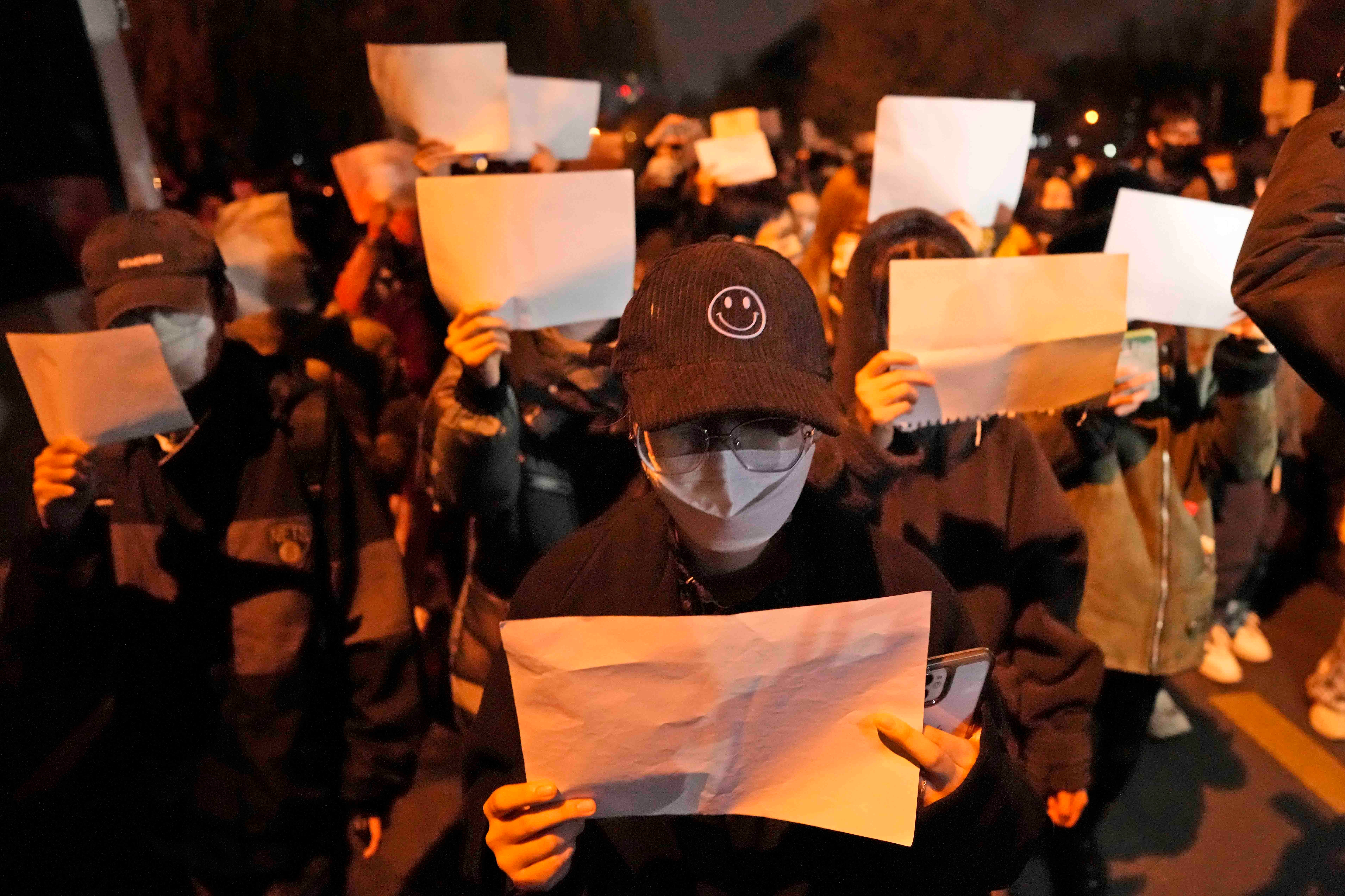 Protesters hold up blank papers and chant slogans as they march in protest in Beijing