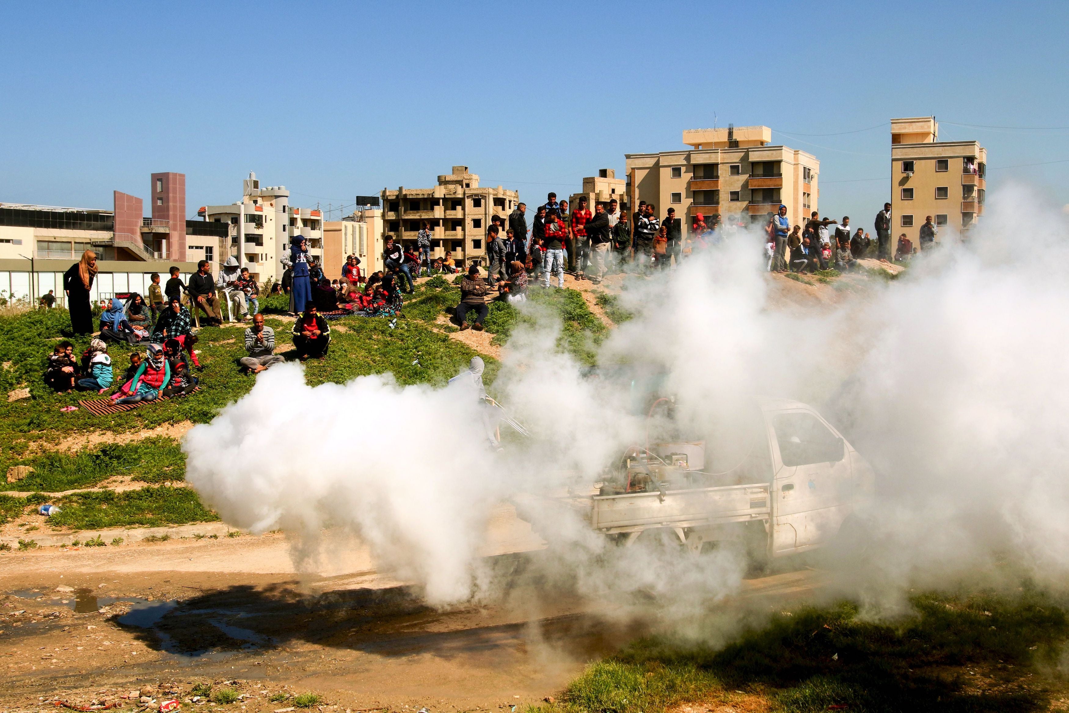 Syrian refugees watch as sanitation workers spray disinfectant near a building under construction they have been using as a shelter in Lebanon's southern city of Sidon amid the spread of Covid-19.