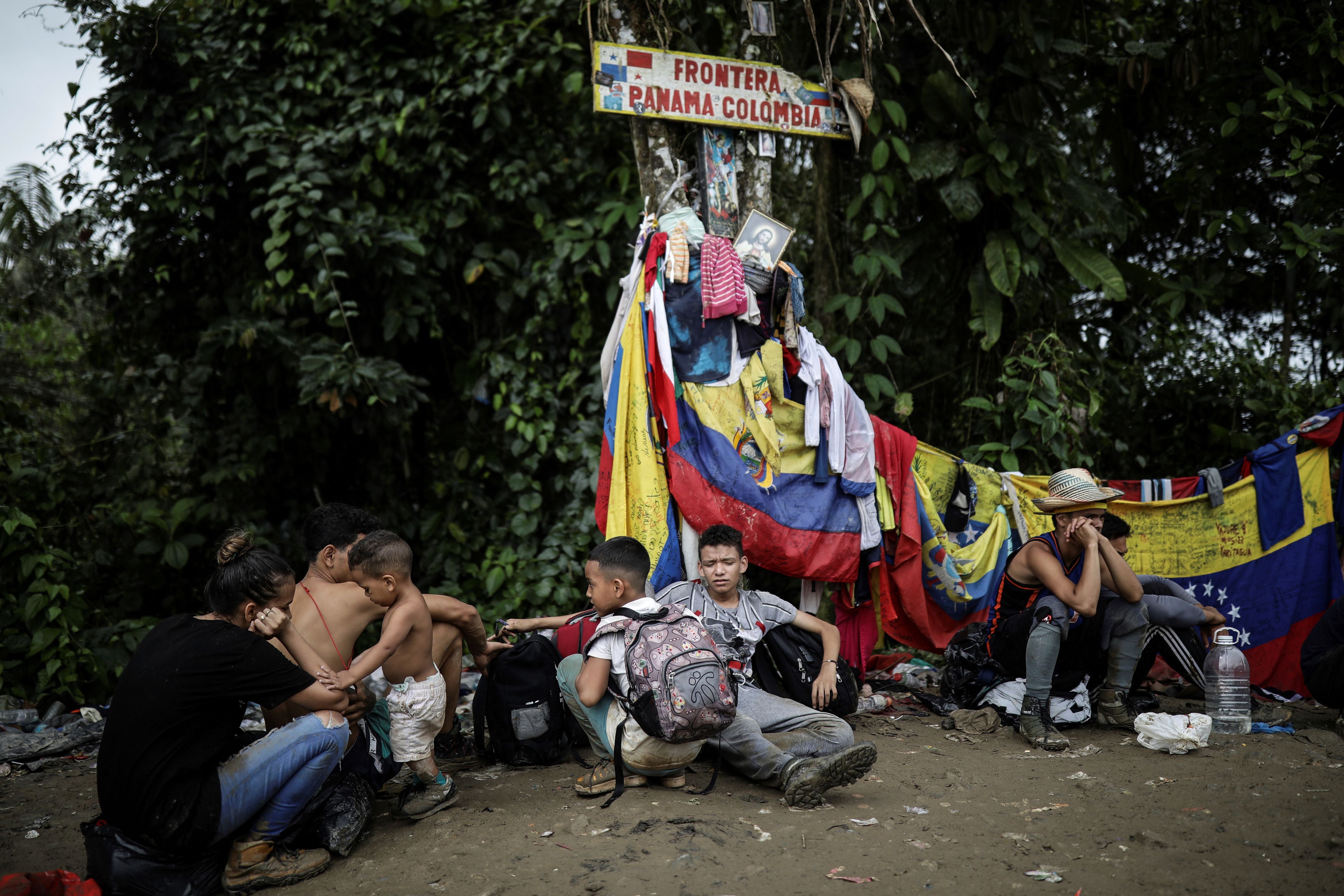 Migrants sit under a sign marking the Panama-Colombia border