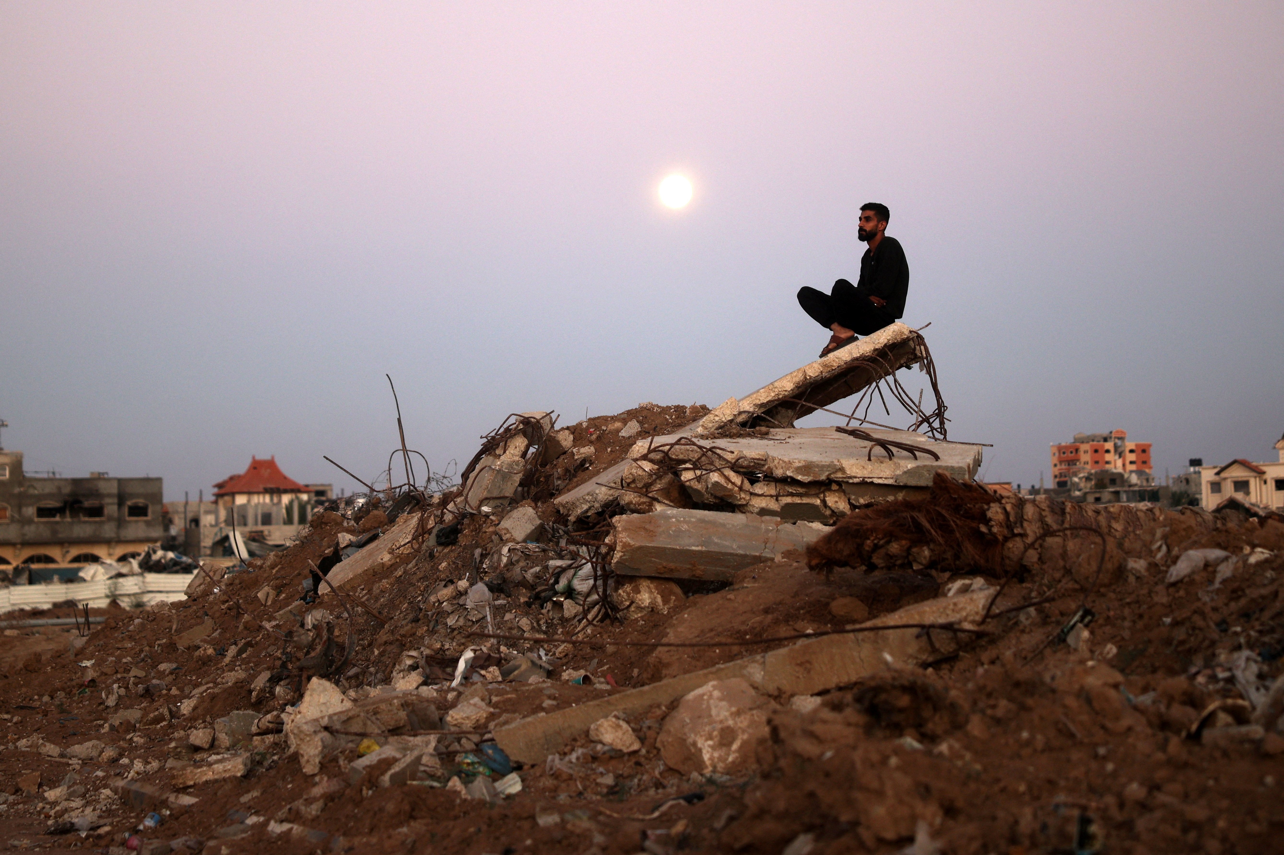 Un hombre sentado sobre una montaña de escombros, con la luna alzándose de fondo, en el campamento de refugiados Al-Bureij en la región central de la Franja de Gaza el 15 de noviembre de 2024, en un contexto de hostilidades en Gaza. 