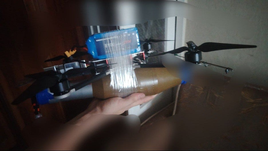 a quadcopter drone with a munition taped to its airframe.