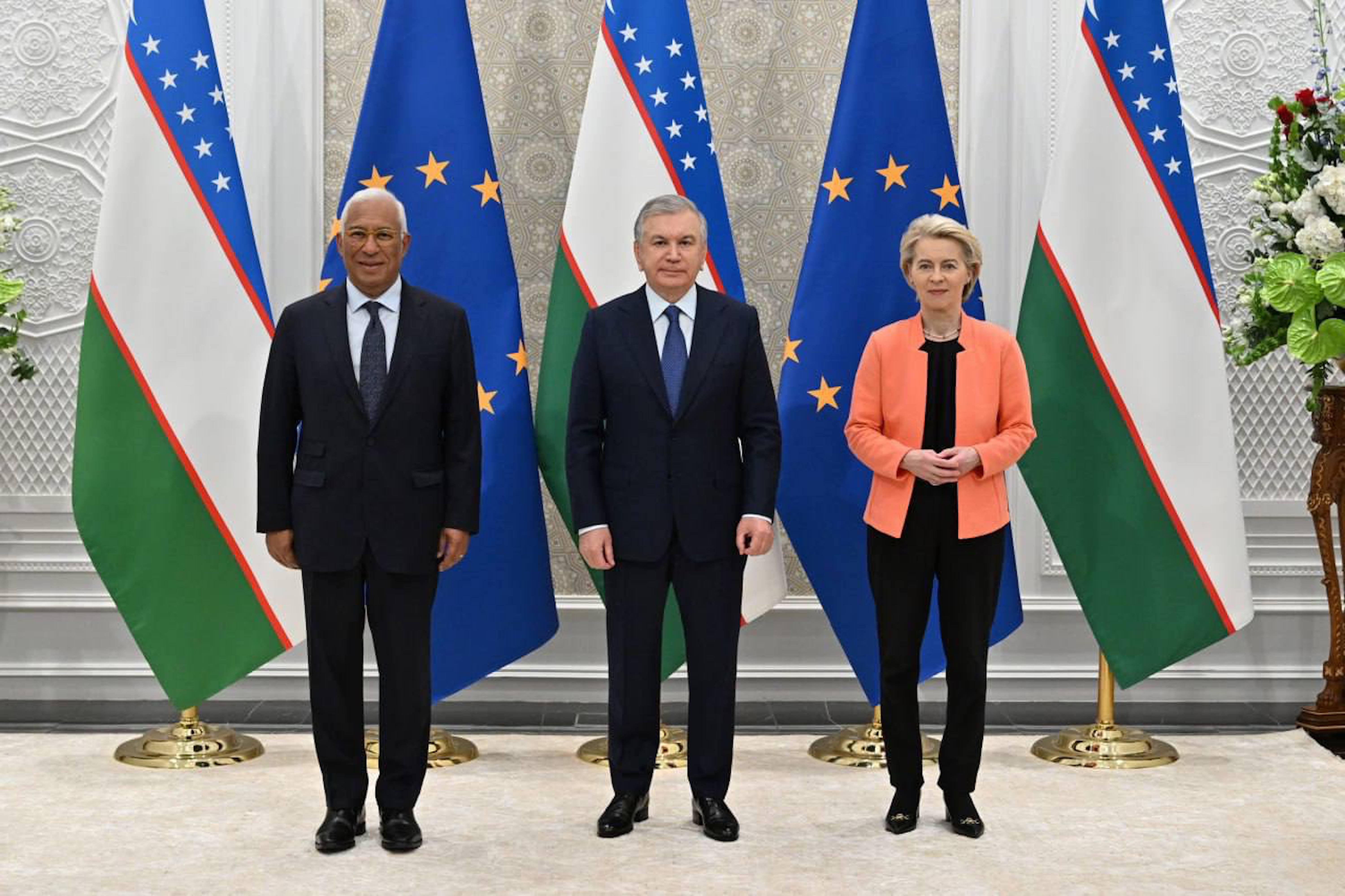 2 men and 1 woman pose for a photo in front of EU and Uzbekistan flags