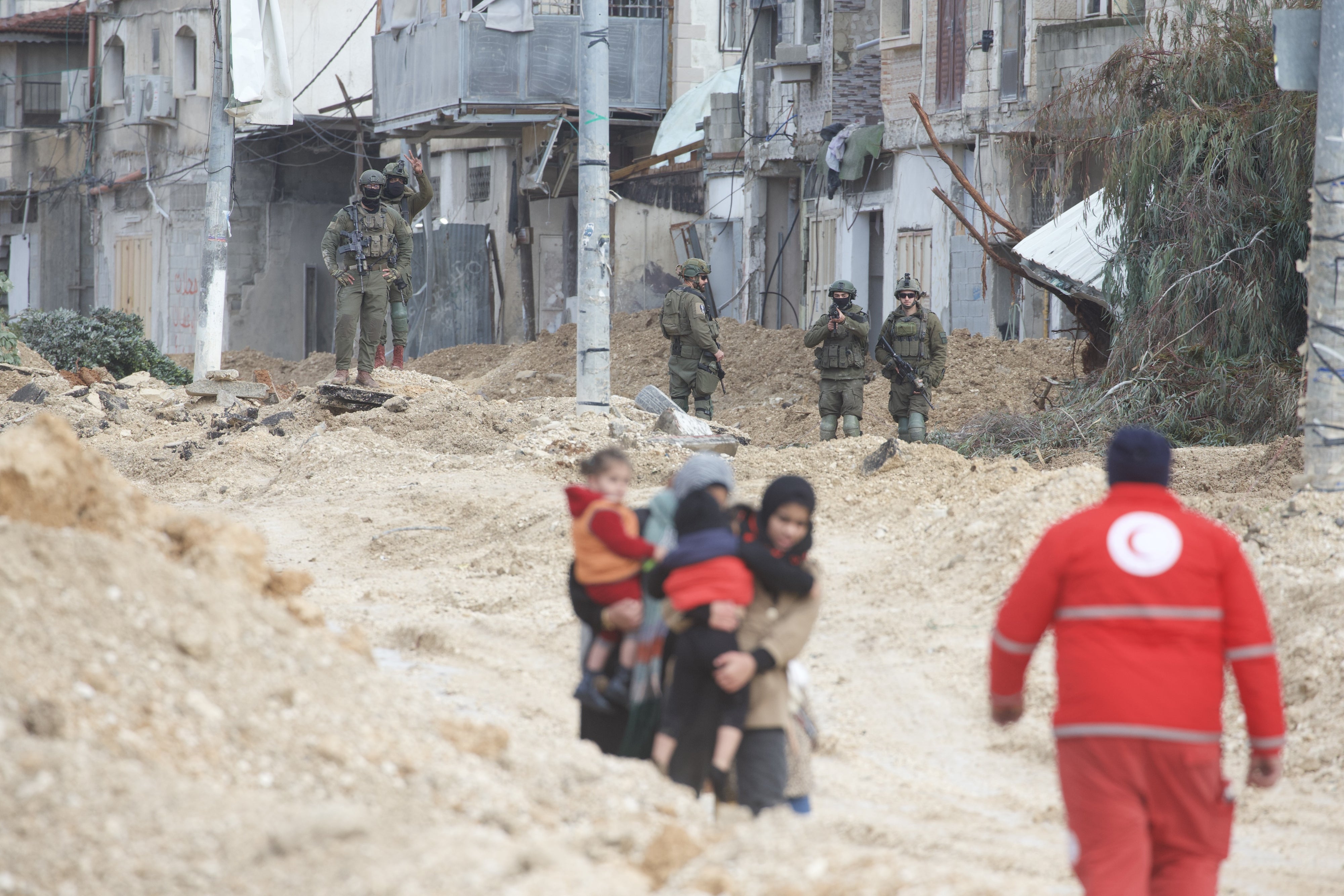 Due donne portano via i bambini durante l’evacuazione forzata del campo profughi di Nur Shams, nel nord della Cisgiordania, sotto gli occhi dei soldati israeliani, uno dei quali ha l’arma puntata. 10 febbraio 2025. © 2025 Wahaj Bani Moufleh
