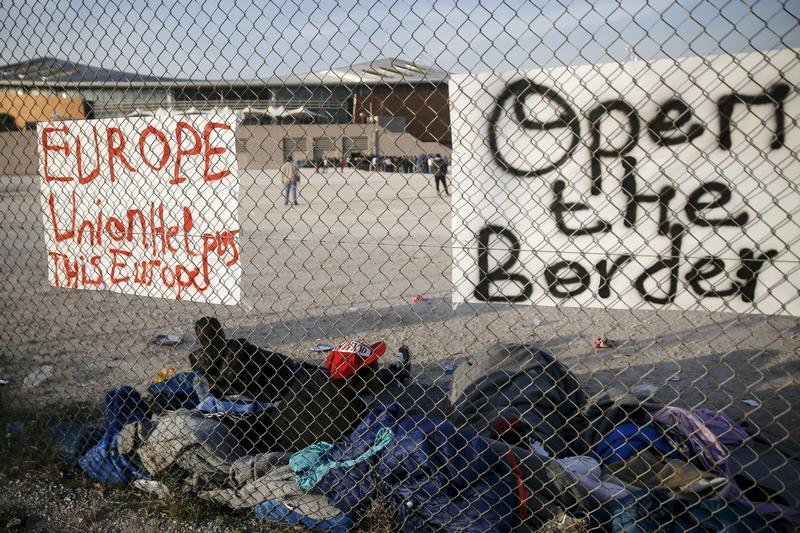 Migrants, who were stranded between Greece and Macedonia, rest next to placards hung on a metal fence, outside the Tae Kwon Do stadium at the southern suburb of Faliro, in Athens, Greece, December 14, 2015. 