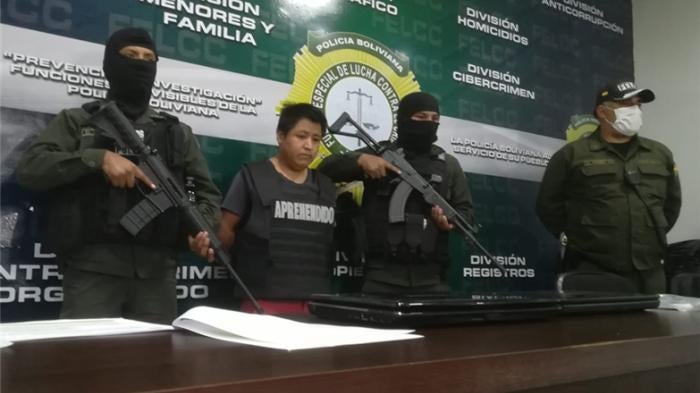 A man stands in front of a desk surrounded by armed soldiers
