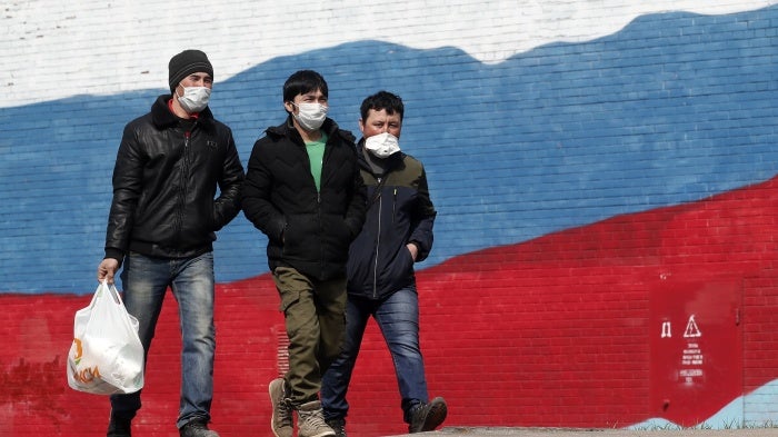 Three men in face masks walk in front of a mural of the Russian flag