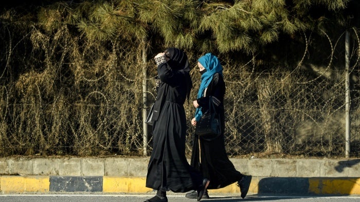 Afghan women walk past razor barricades along a roadside in Kabul on December 8, 2024.