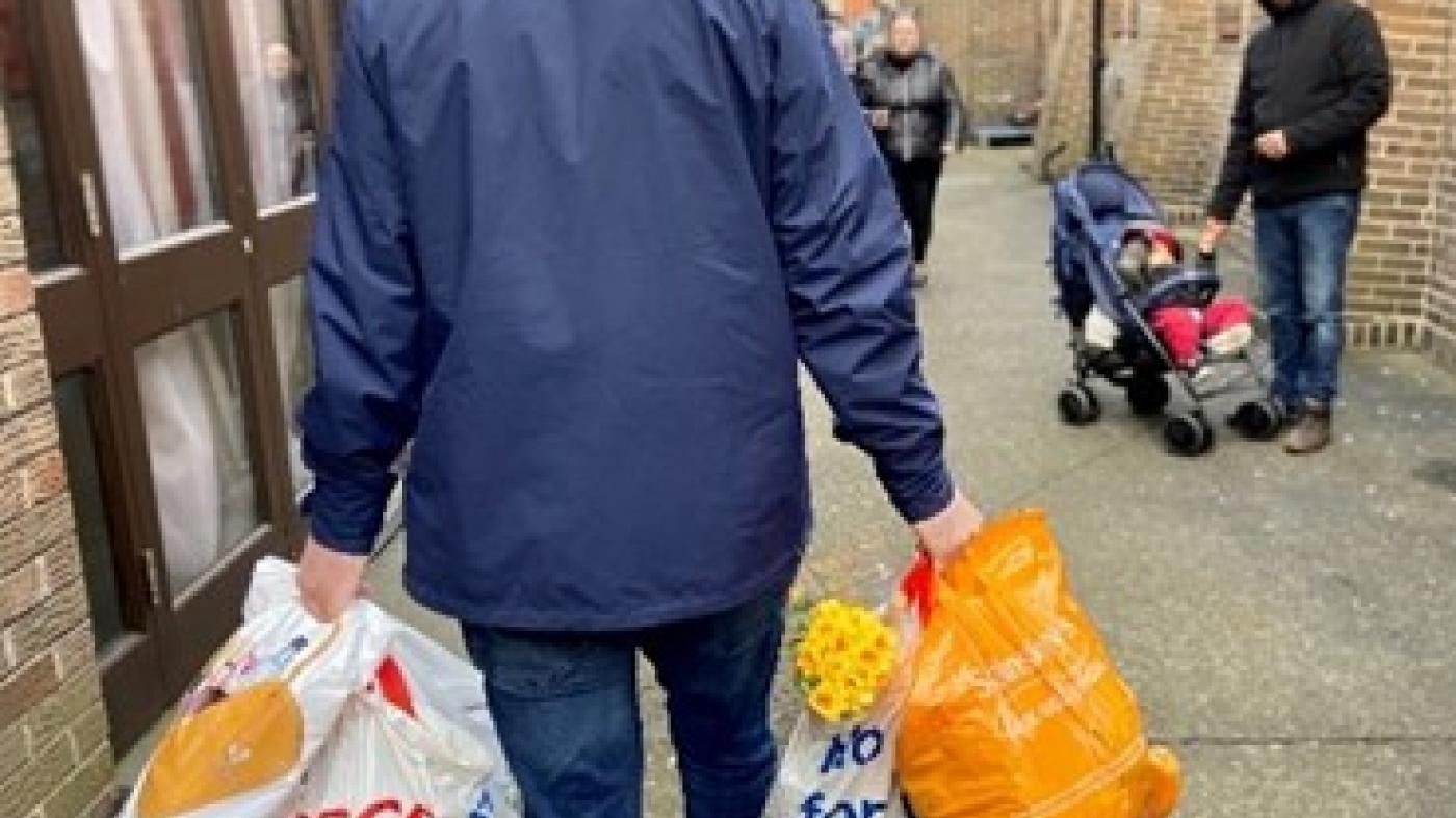 A man in a coat walks down a street carrying grocery bags