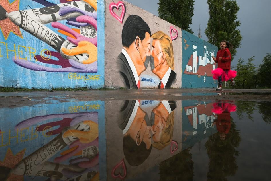 A girl runs in front of graffiti depicting US President Trump and China's President Xi Jinping with face masks displayed on a wall in Berlin, Germany, April 29, 2020.