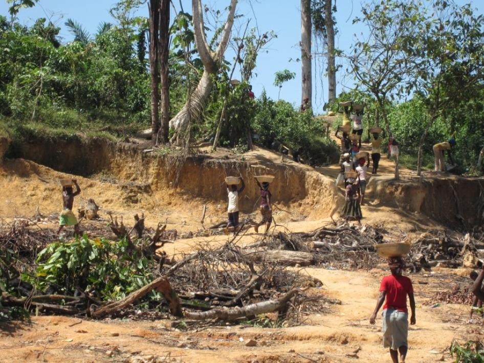 A wide shot of people carrying pans on their heads in a mining site