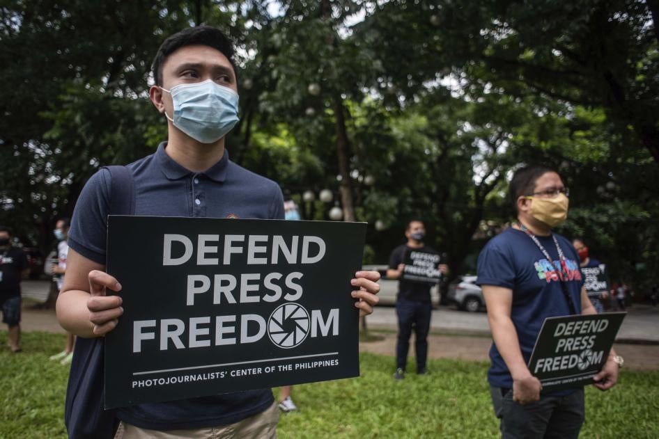 People in face masks hold signs that read "Defend Press Freedom"