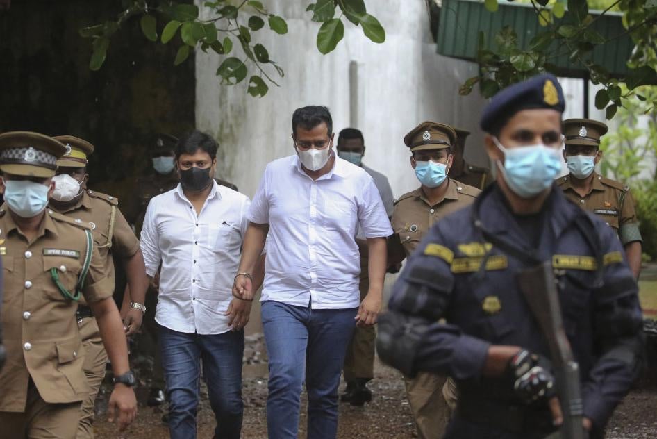 Two Sri Lankan parliamentarians walk to prison bus escorted by officers.