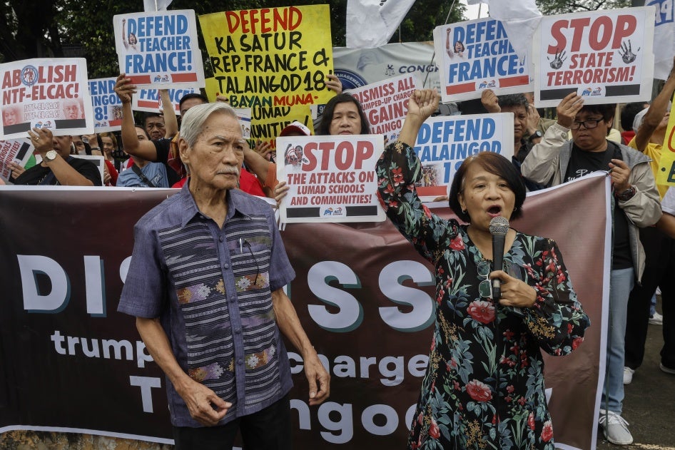 A man and a woman hold microphones in front of a crowd holding protest banners