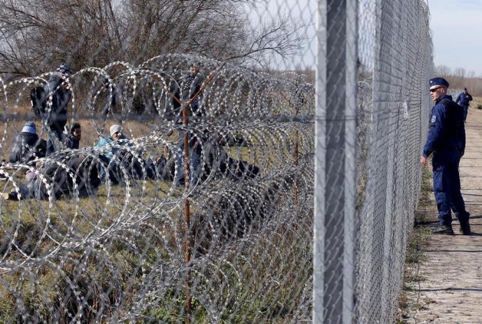 Migrants rest as a policeman watches them near Hungary's border fence on the Serbian side of the border near Morahalom, Hungary, February 22, 2016.