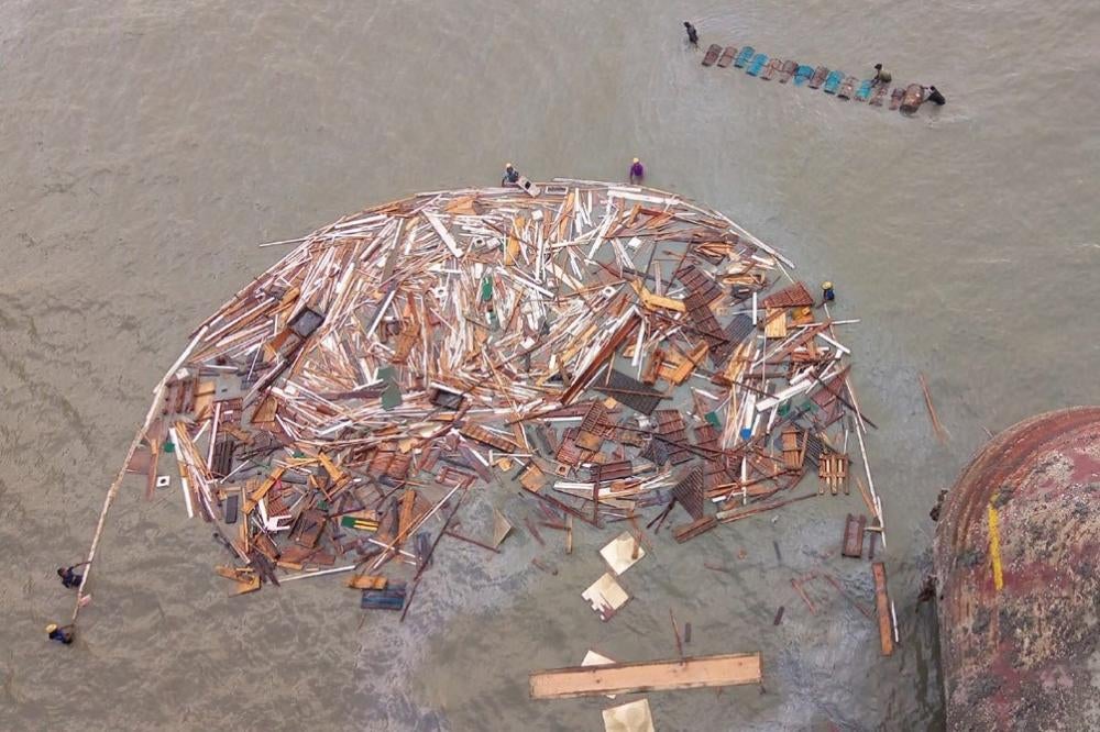 Shipbreaking workers wade in the water to collect remnants of a broken ship. 