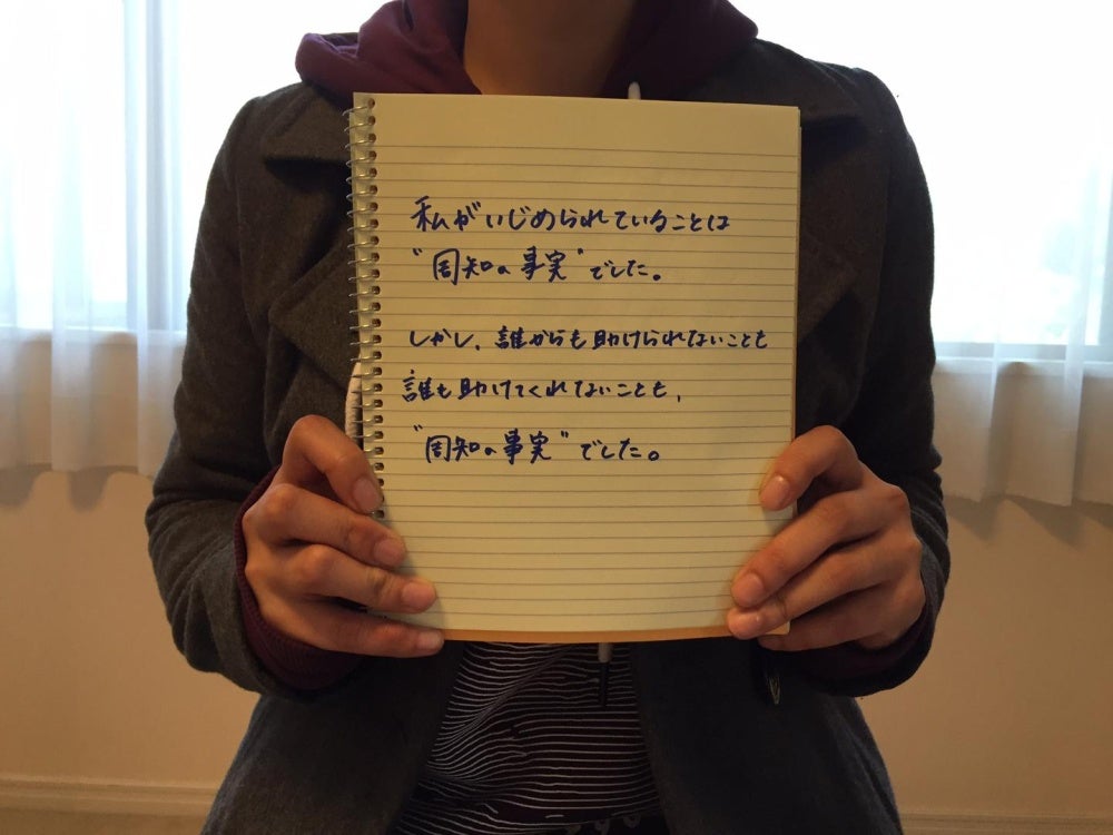 A 20-year-old Japanese woman who was bullied by her classmates in junior high school holds a notebook displaying the message: “It was common knowledge that I was being bullied. It was also common knowledge that my teachers would never help me.” 