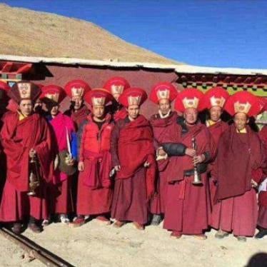 A row of monks in red outfits and headdresses pose for a photo