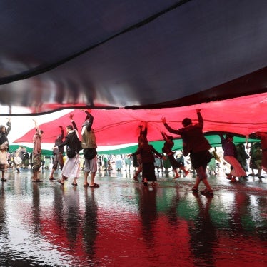 People stand beneath large flags at a protest
