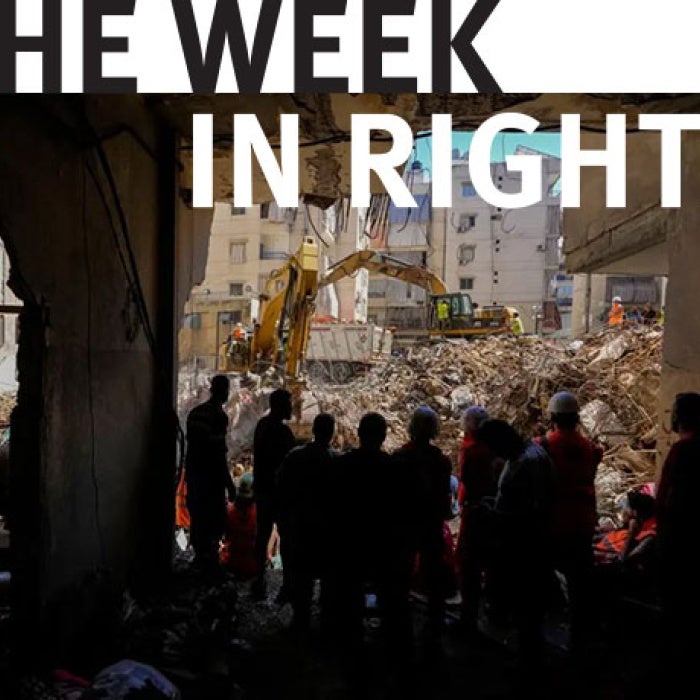 Onlookers stand in front of rubble. 