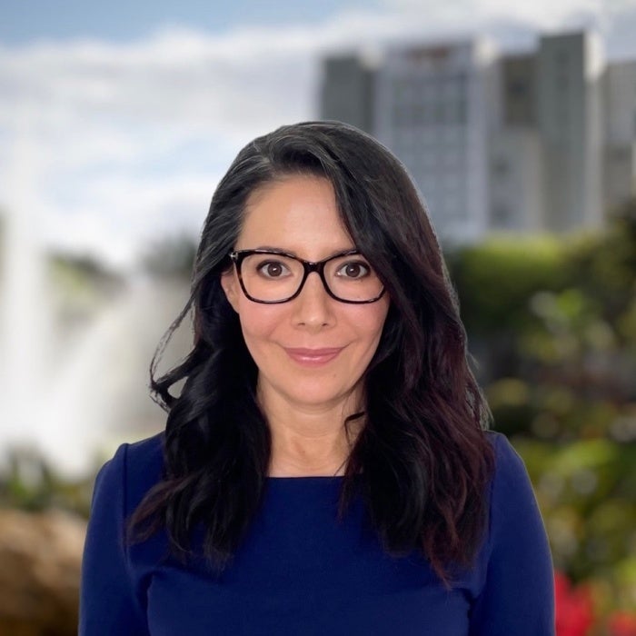 A woman with long dark hair and reading glasses